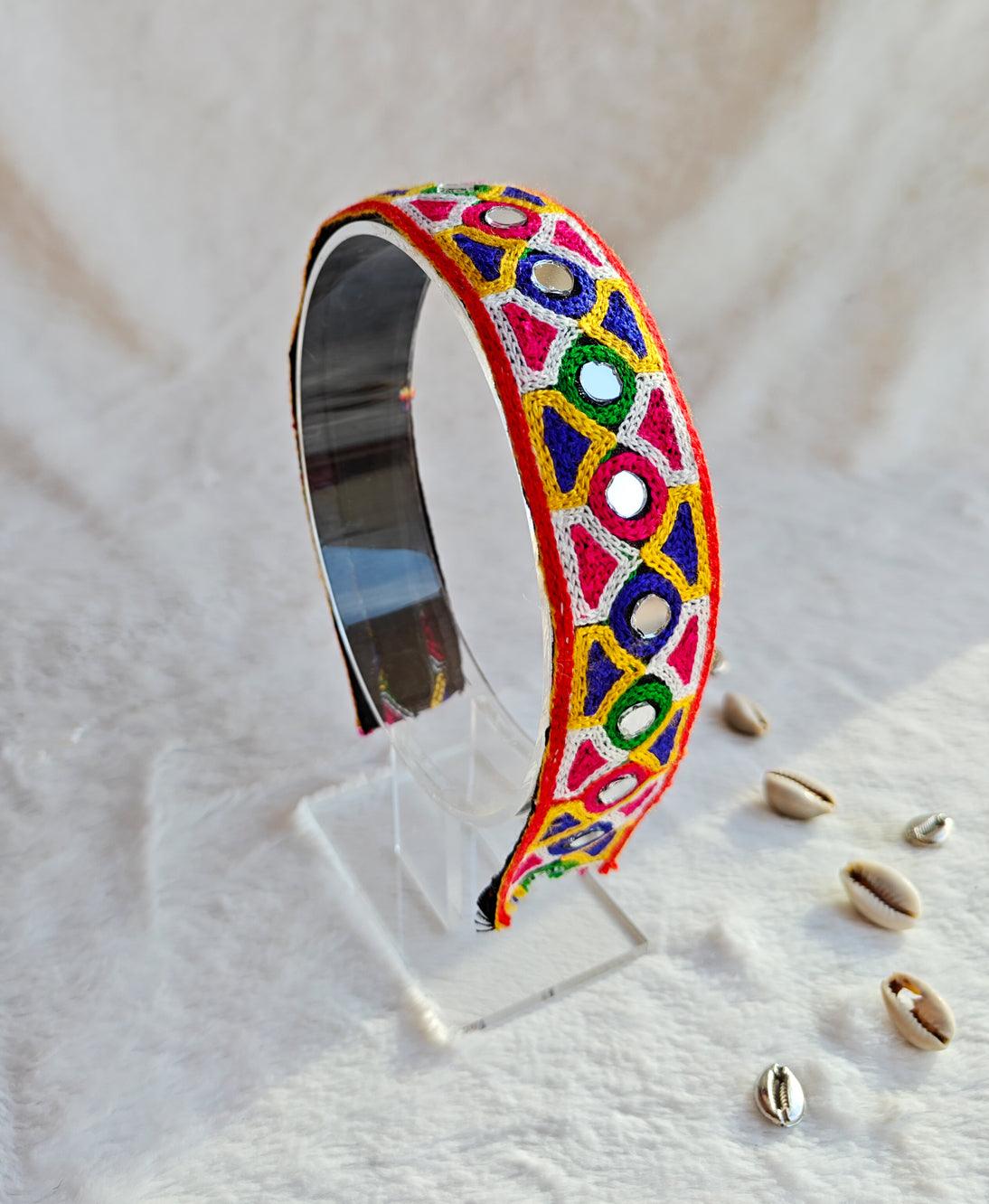 Festive Navratri headband with vibrant embroidered geometric patterns in pink, yellow, green, and blue, displayed on a clear stand.