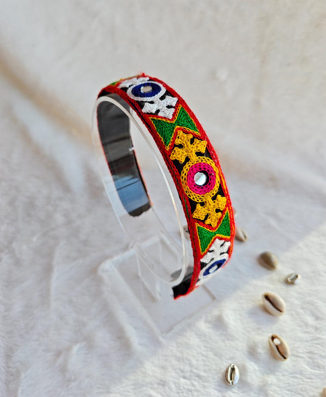 Colorful Navratri headband featuring intricate embroidered designs with vibrant geometric patterns in yellow, green, red, and white, displayed on a clear stand. Main image